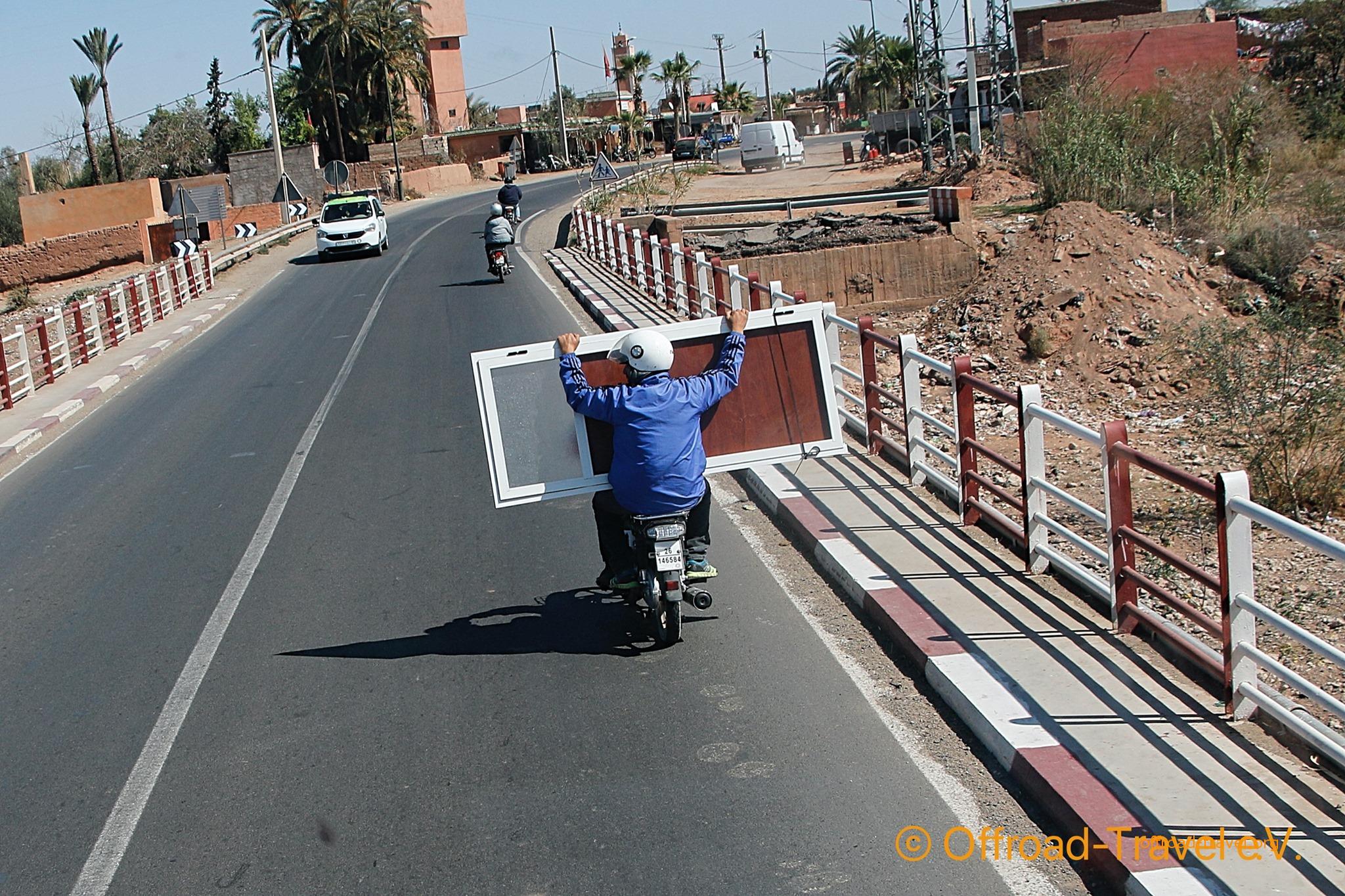 Auf den Straßen von Marokko. Eine Person fährt das Moped und der Mitfahrer hält eine Tür, die so transportiert wurde.